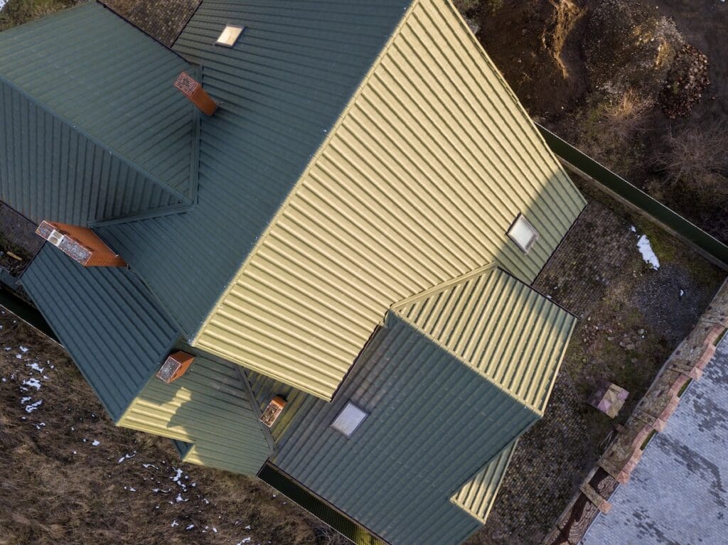 Aerial view of new residential house cottage with shingle roof on fenced yard on sunny day.